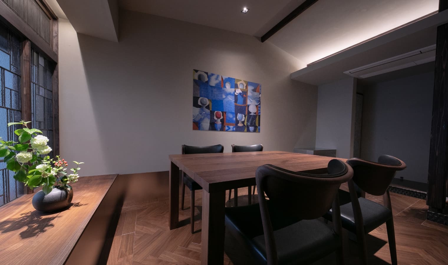 Private dining room with a walnut table, ikebana arrangement and herringbone wood floor