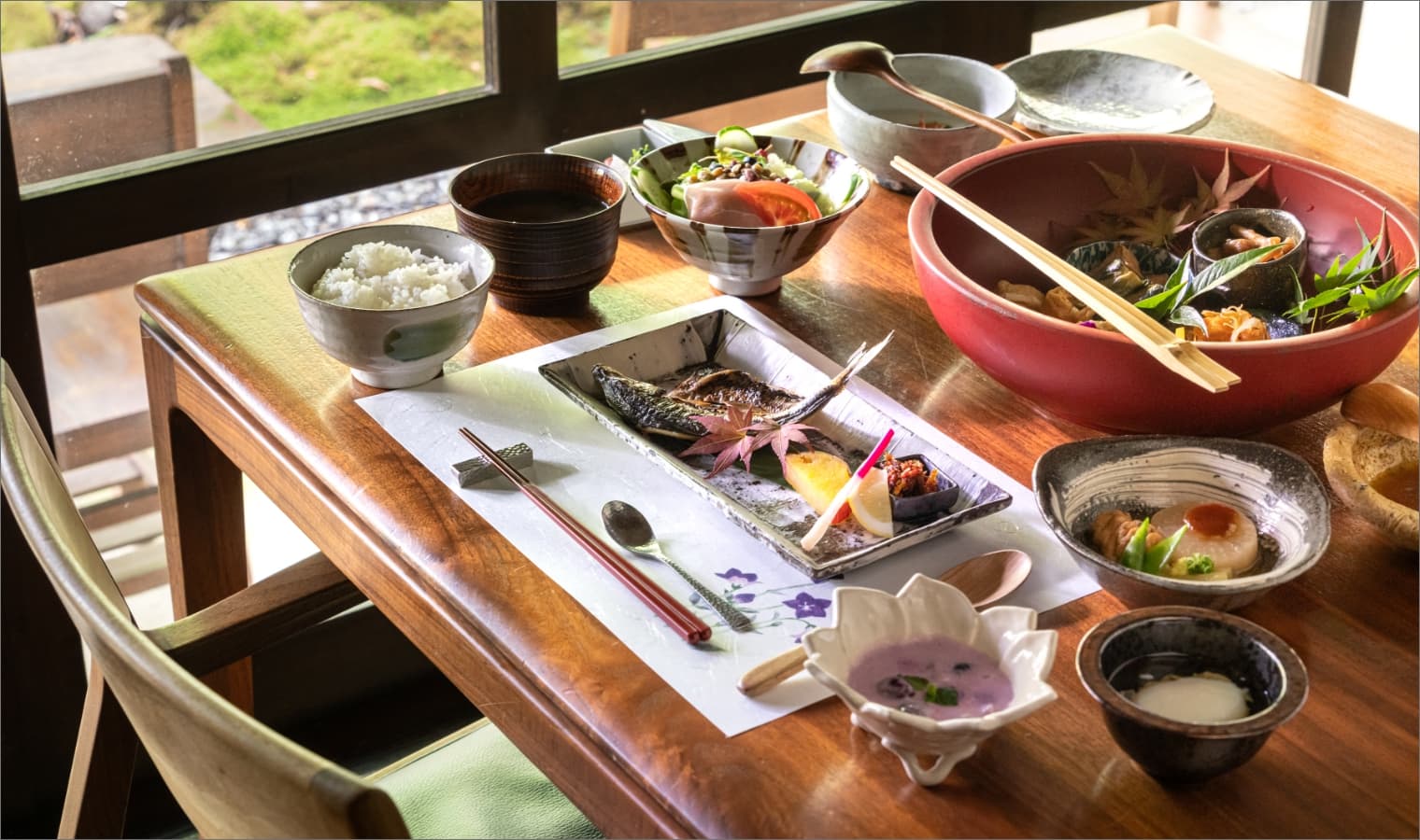Japanese breakfast set with grilled fish, rice, miso soup and small dishes by a garden-view window