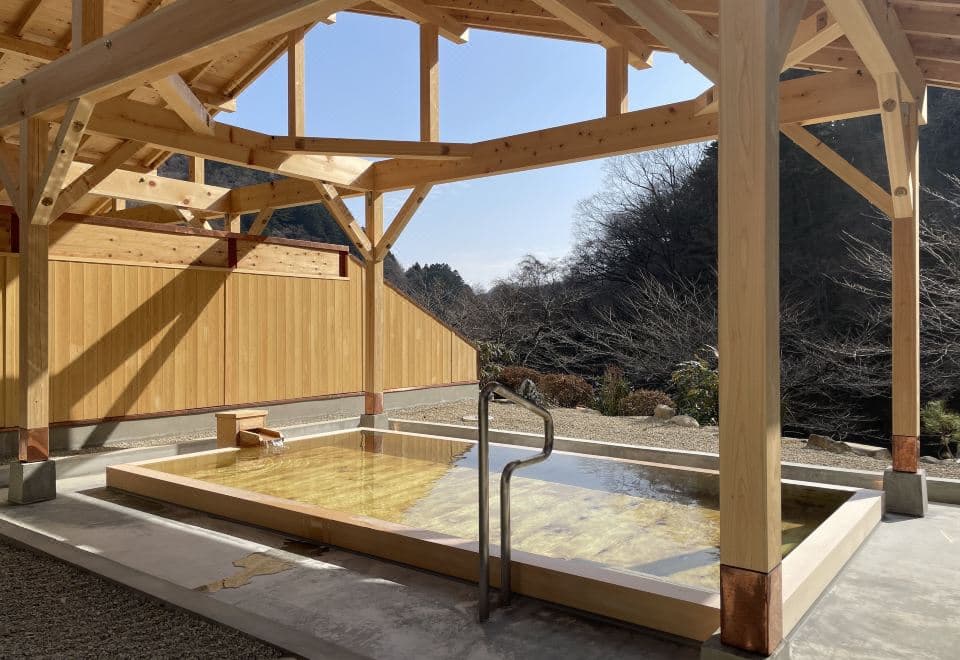 Open-air hot spring bath of yellow mineral water under a wooden pavilion