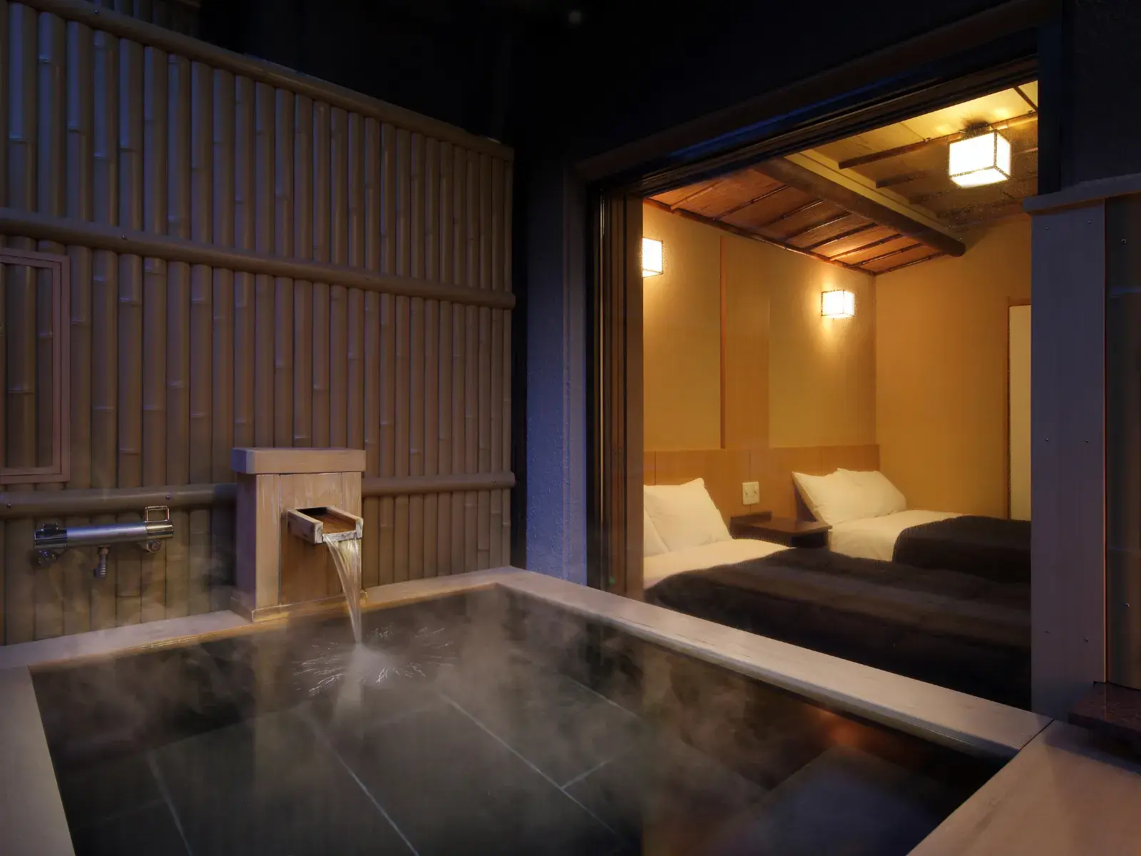 Guest room with a private open-air bath beside a twin-bed room at night
