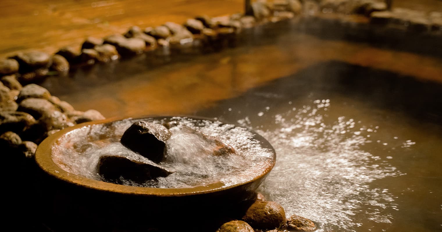 Steam rising over the natural amber onsen water and stone basin in the bathhouse at Bettei Amafuru Oka, Ibusuki