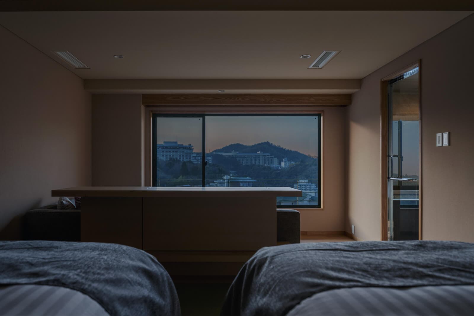 Twin-bed premium guest room with a corner picture window framing the Arima Onsen mountains at dusk at Takayamaso Hanano