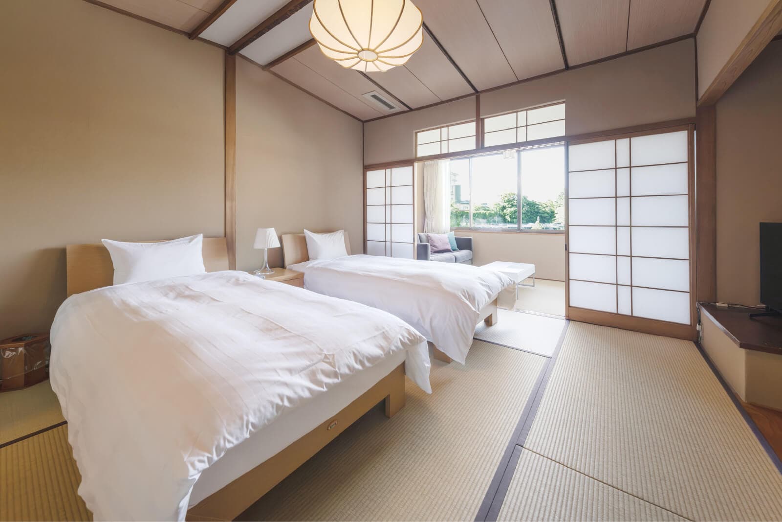 Bright tatami guest room with twin Western beds and shoji screens opening to a sunlit window seat at Takayamaso Hanano, Arima Onsen