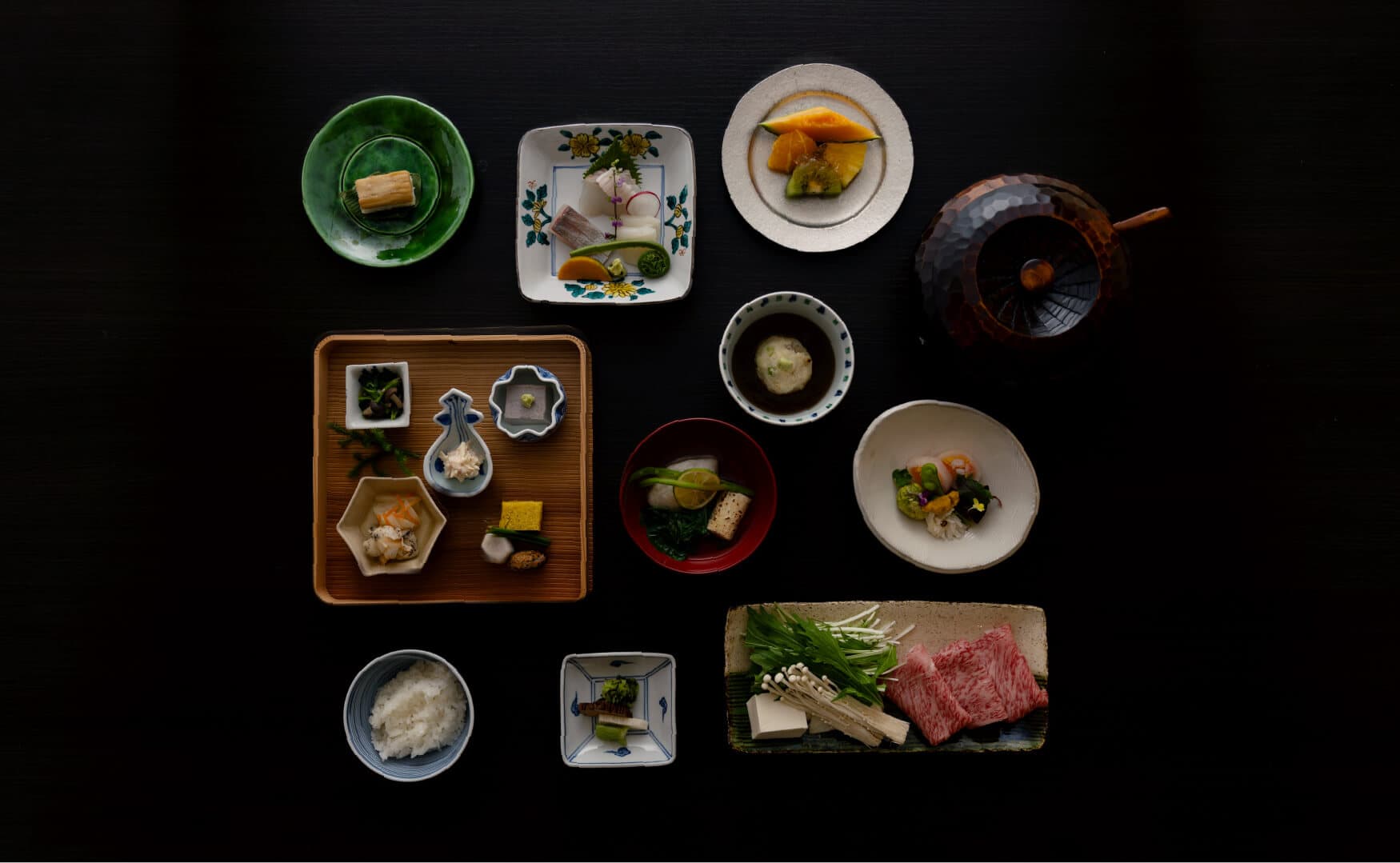 Overhead view of a multi-course seasonal kaiseki dinner spread with sashimi, simmered dishes and Kobe beef at Takayamaso Hanano, Arima Onsen