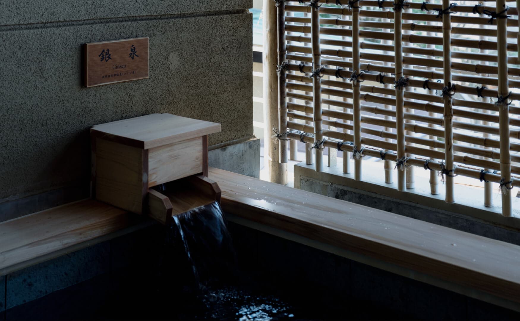 Ginsen silver-spring bath with clear water pouring from a wooden spout beside a bamboo lattice screen at Takayamaso Hanano, Arima Onsen