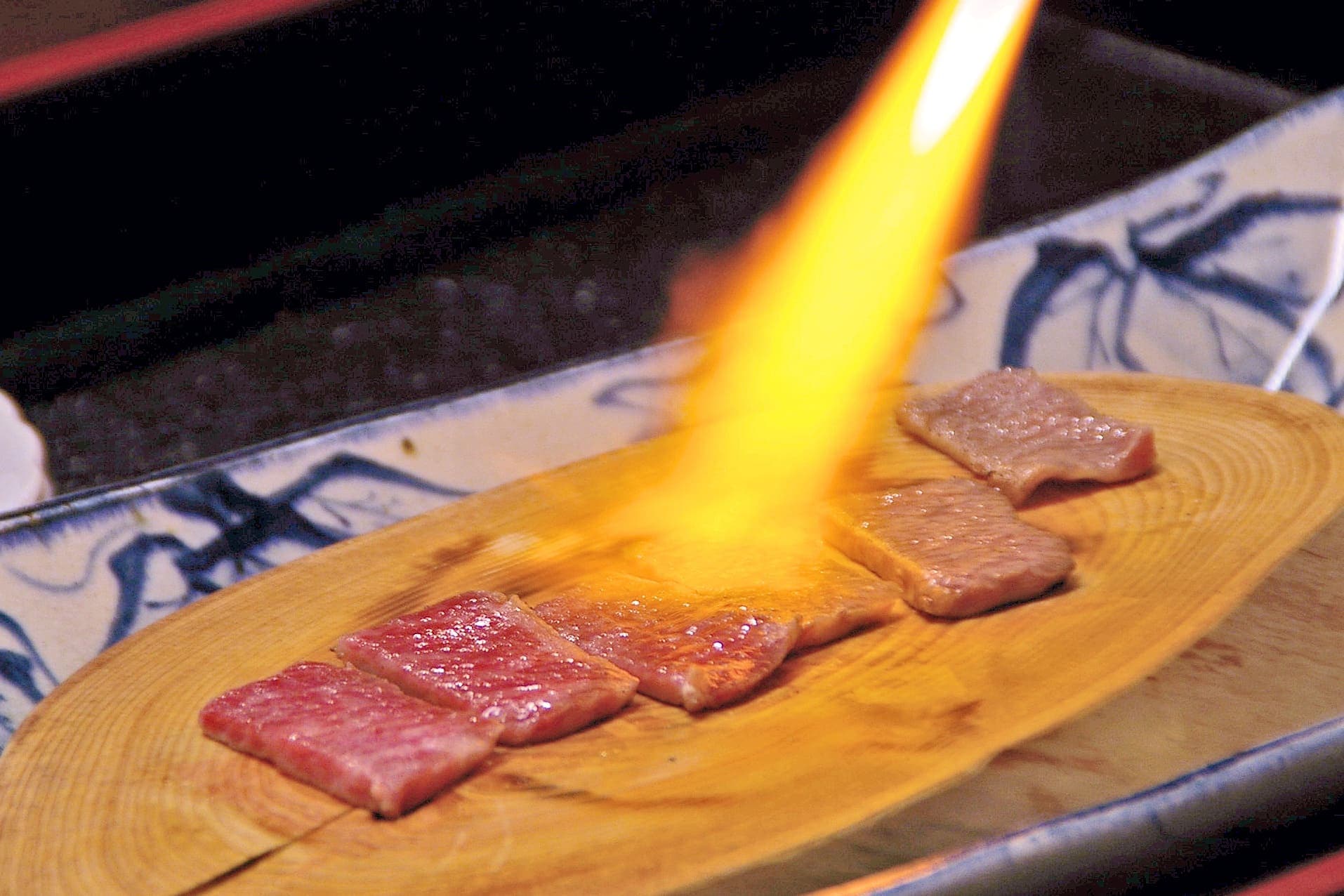 Hatago kaiseki course of premium wagyu beef seared tableside over open flame on a wooden board