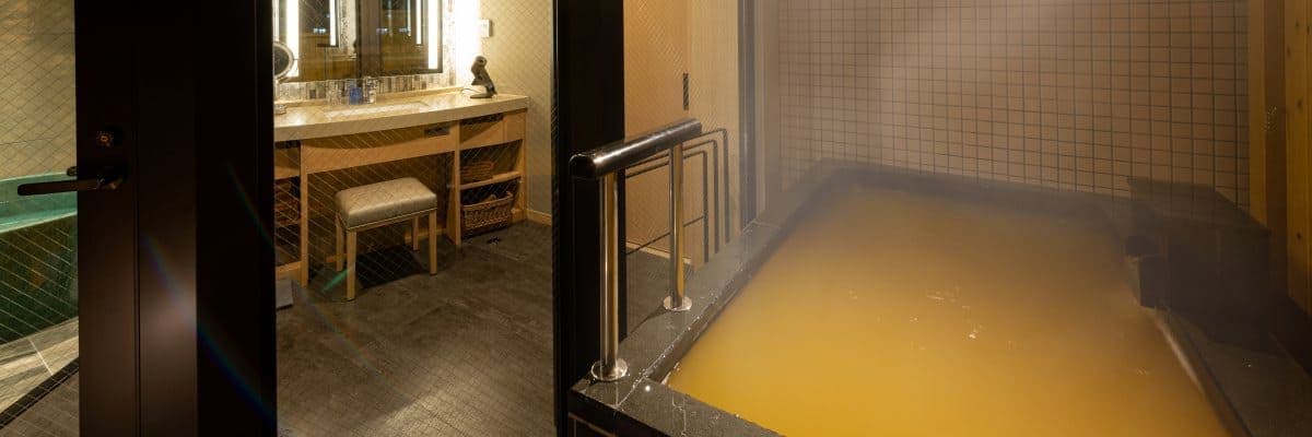 Hatago in-room indoor kinsen bath with steaming gold-spring water beside a tiled vanity counter