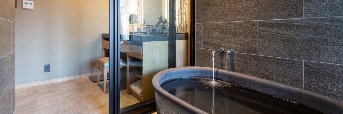 Hatago in-room private bath with a deep black ceramic ginsen tub, running spout and stone-tiled wall