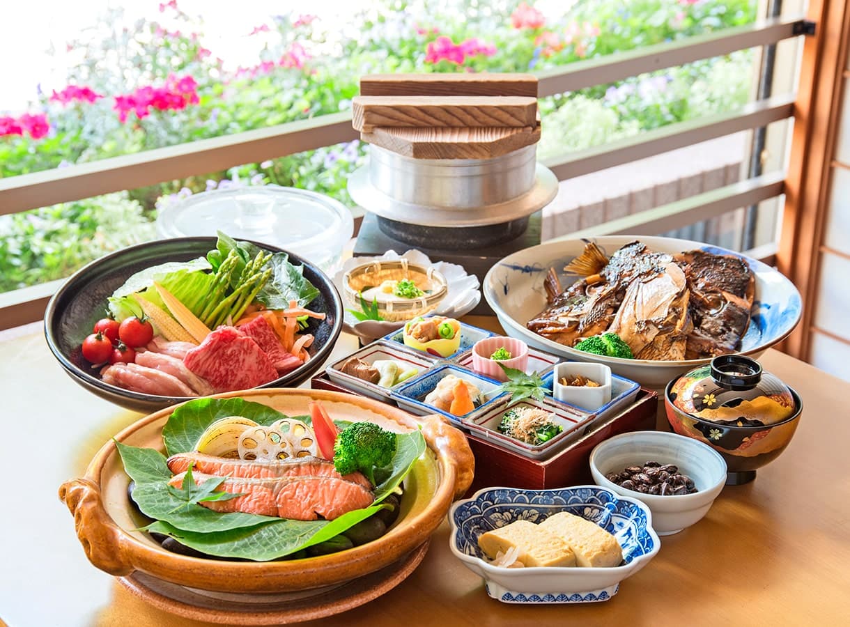 Multi-course kaiseki dinner spread at Oku no Hosomichi with wagyu hot pot, grilled fish and assorted dishes set by a window of pink blossoms