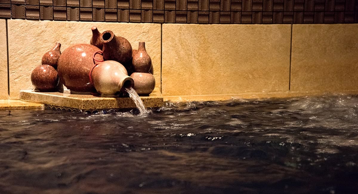 Detail of reddish Arima kinsen water pouring from ceramic gourd jars into a stone bath at Oku no Hosomichi