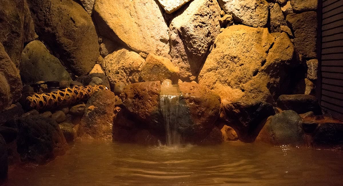 Tenchi no Yado Oku no Hosomichi indoor kinsen bath with reddish-brown iron-rich Arima hot spring water flowing over a natural rock cascade