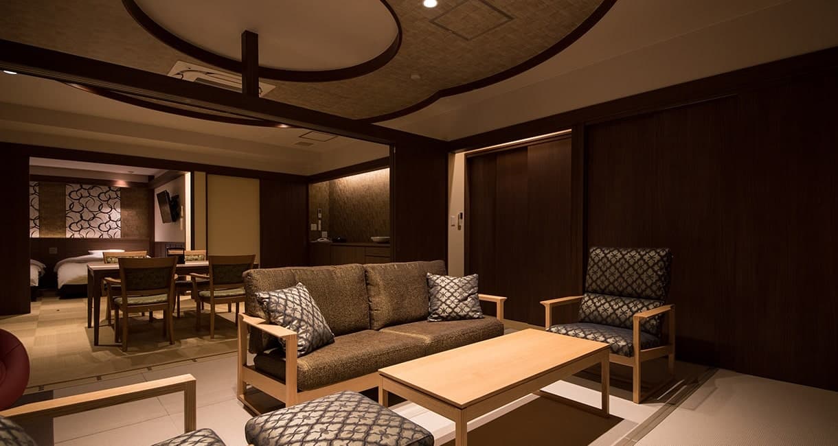 Spacious annex suite living lounge at Oku no Hosomichi with sofa seating, bamboo-slat ceiling and bedroom beyond at dusk