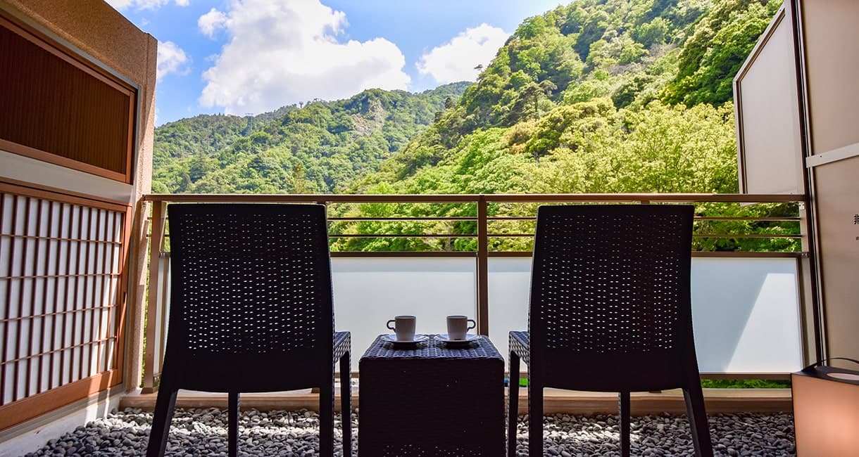 Guest room balcony at Oku no Hosomichi with two chairs framing a green forested mountain view of Arima
