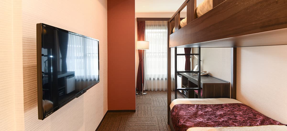Koki bunk-bed guest room with a wooden upper berth, wall-mounted TV and work desk