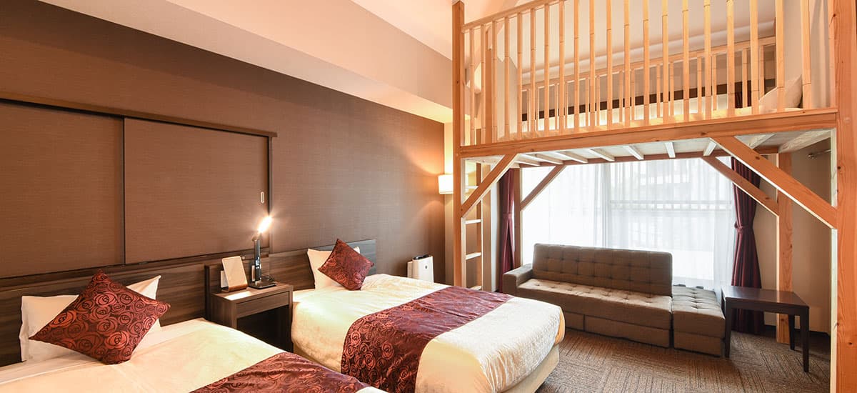 Koki loft twin guest room with twin beds below a wooden mezzanine loft and a sofa seating nook
