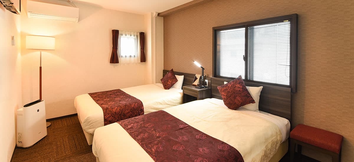 Koki compact small twin guest room with two beds, floor lamp and warm cream walls