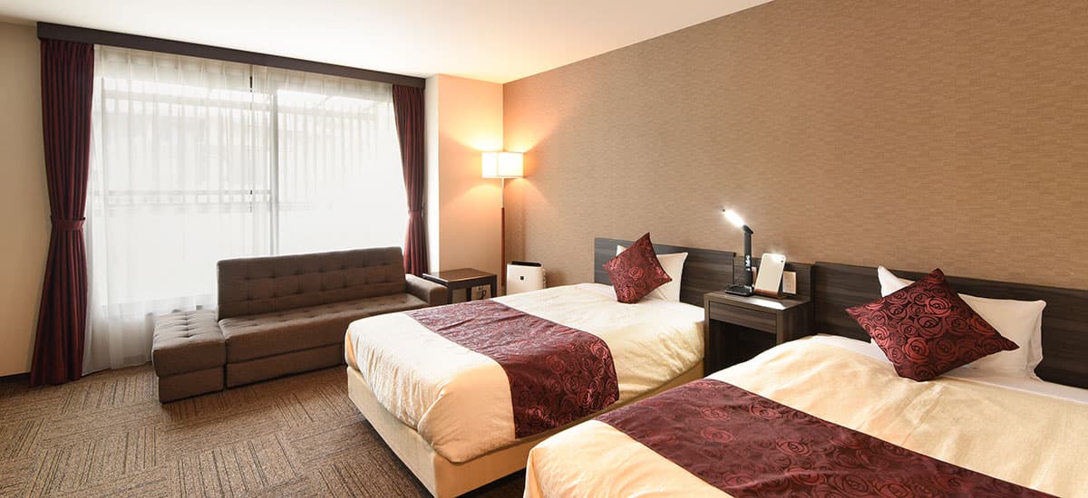 Koki twin guest room with two beds, a brown sofa and floor lamp against a textured taupe wall
