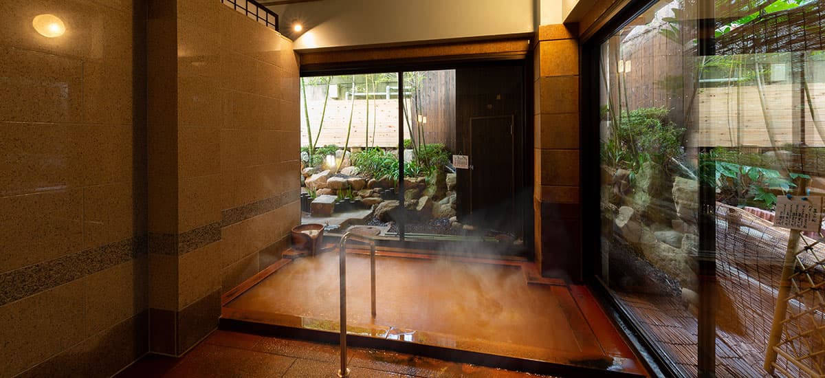 Koki indoor kinsen bath with rising steam and a small Japanese garden viewed through the window