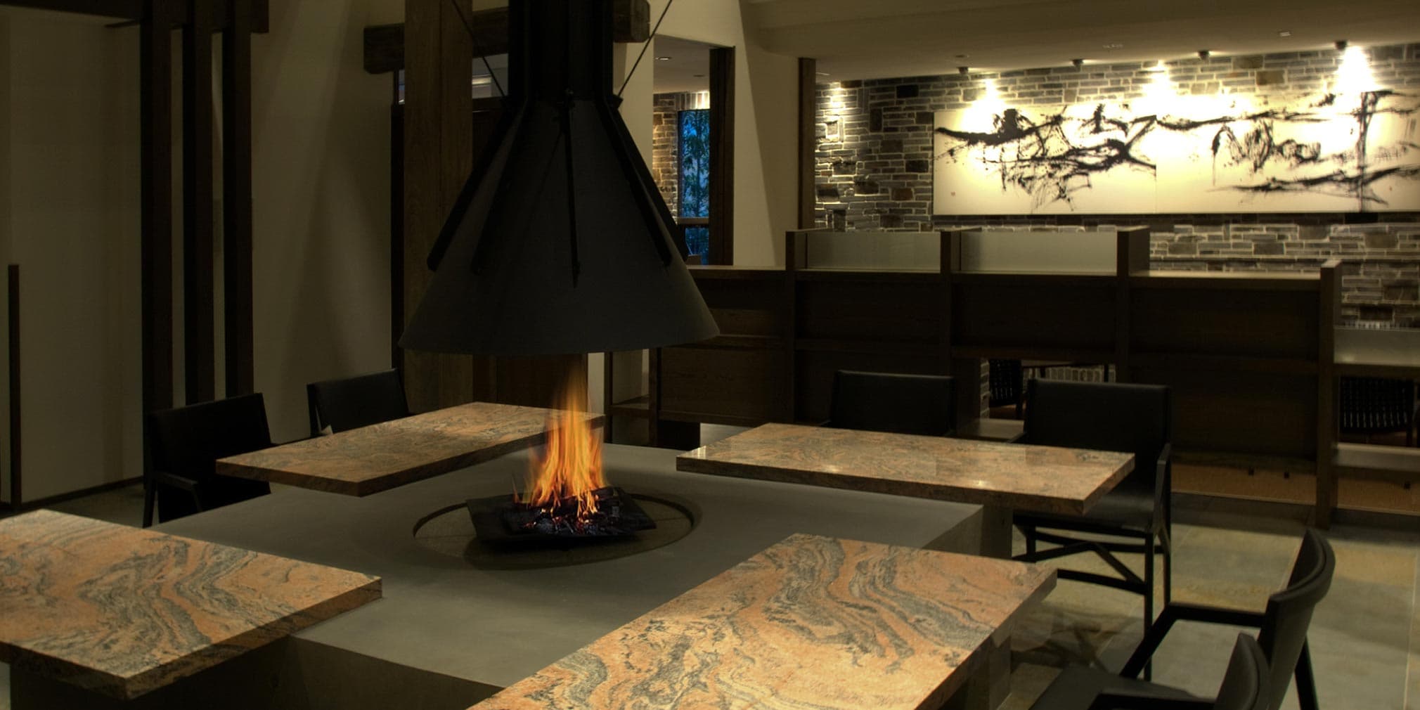 Dining hall with a central open fire pit and stone-tile tables at Yufuin Bettei Itsuki