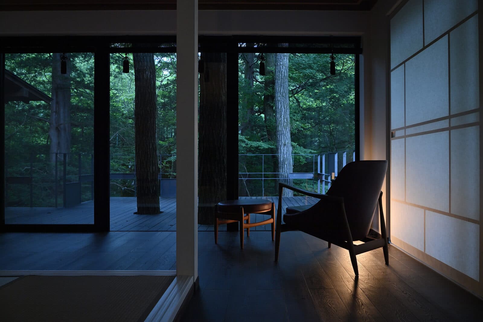 Guest room lounge chair beside floor-to-ceiling forest windows