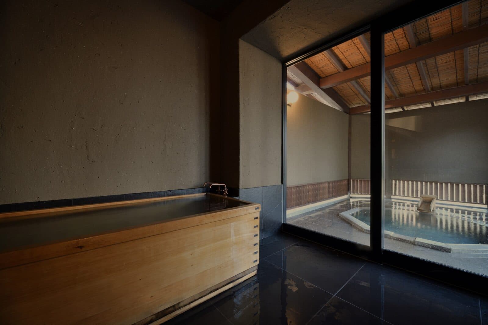 Private in-room hinoki wood tub beside a stone bath and forest view