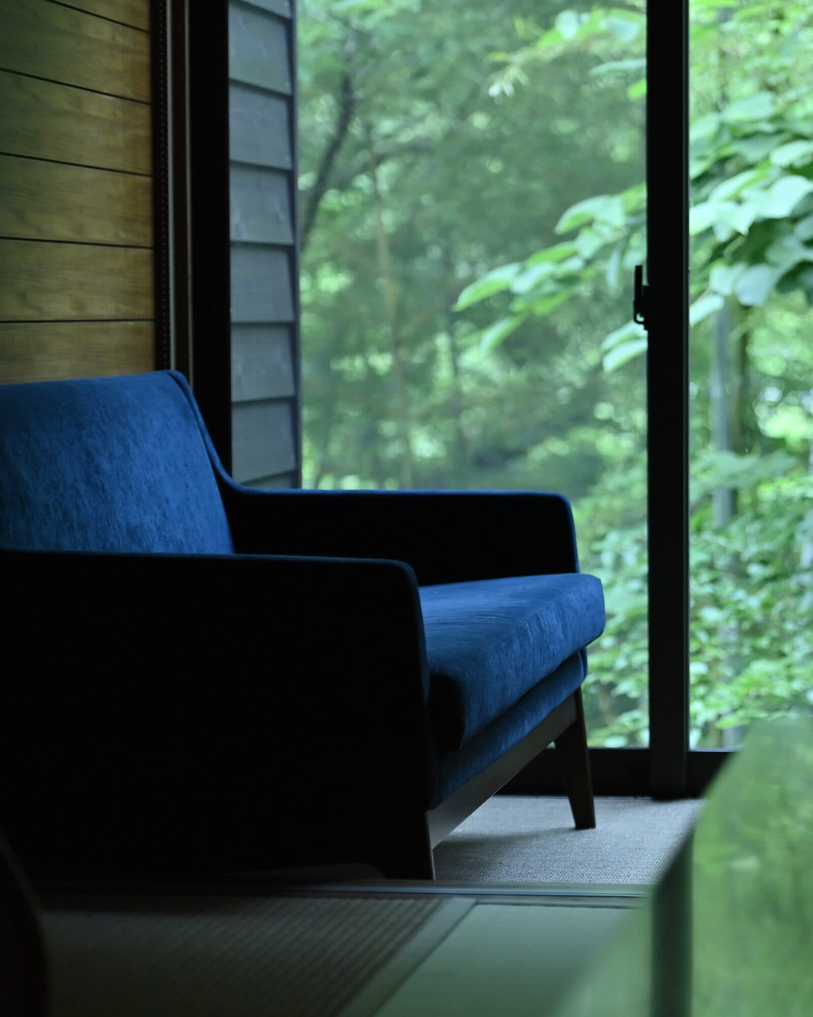 Blue velvet armchair set against a green forest window