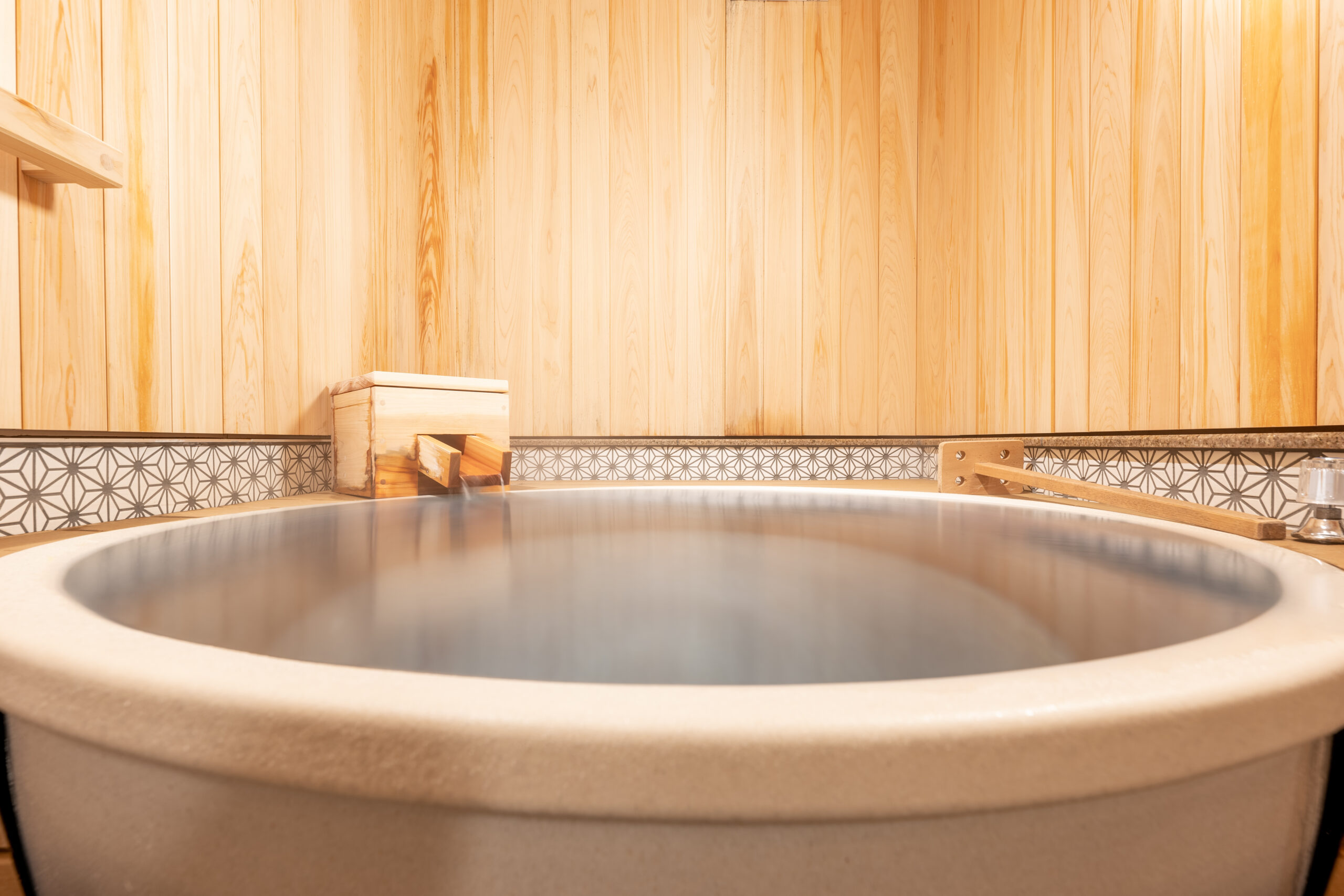 Round soaking tub filled with milky onsen water against a hinoki plank wall