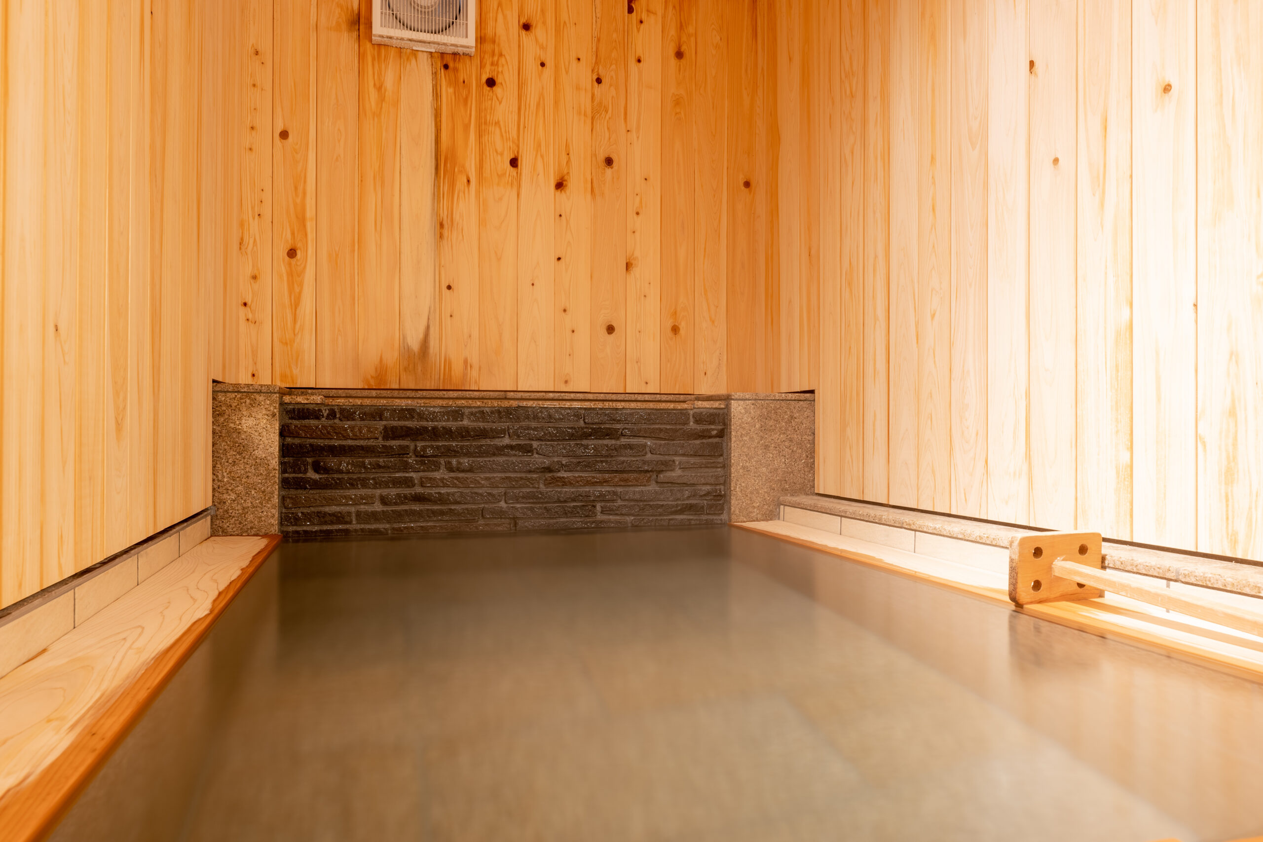 Wide private bath floor framed by cedar walls and a dark stone accent band