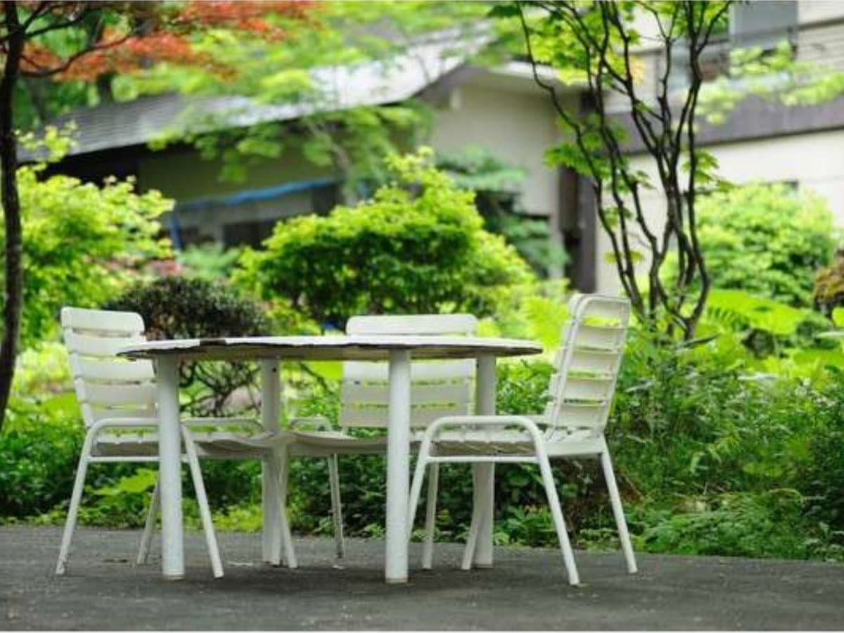 Garden terrace with white table and chairs among green foliage at Zenshichinoyu Ohira, Zao Onsen