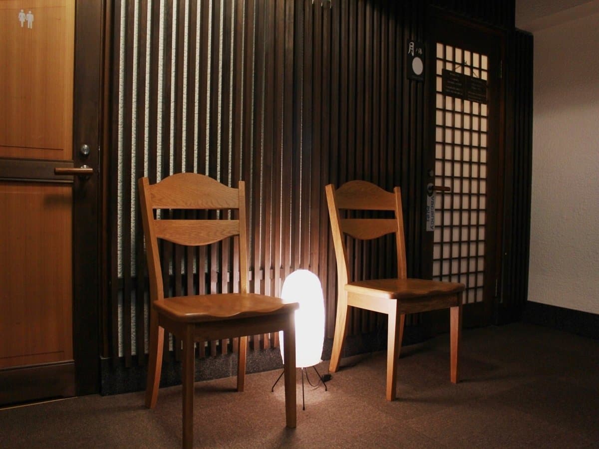 Quiet bath-corridor nook with two wooden chairs and a glowing floor lamp, Koyado En, Kinosaki Onsen
