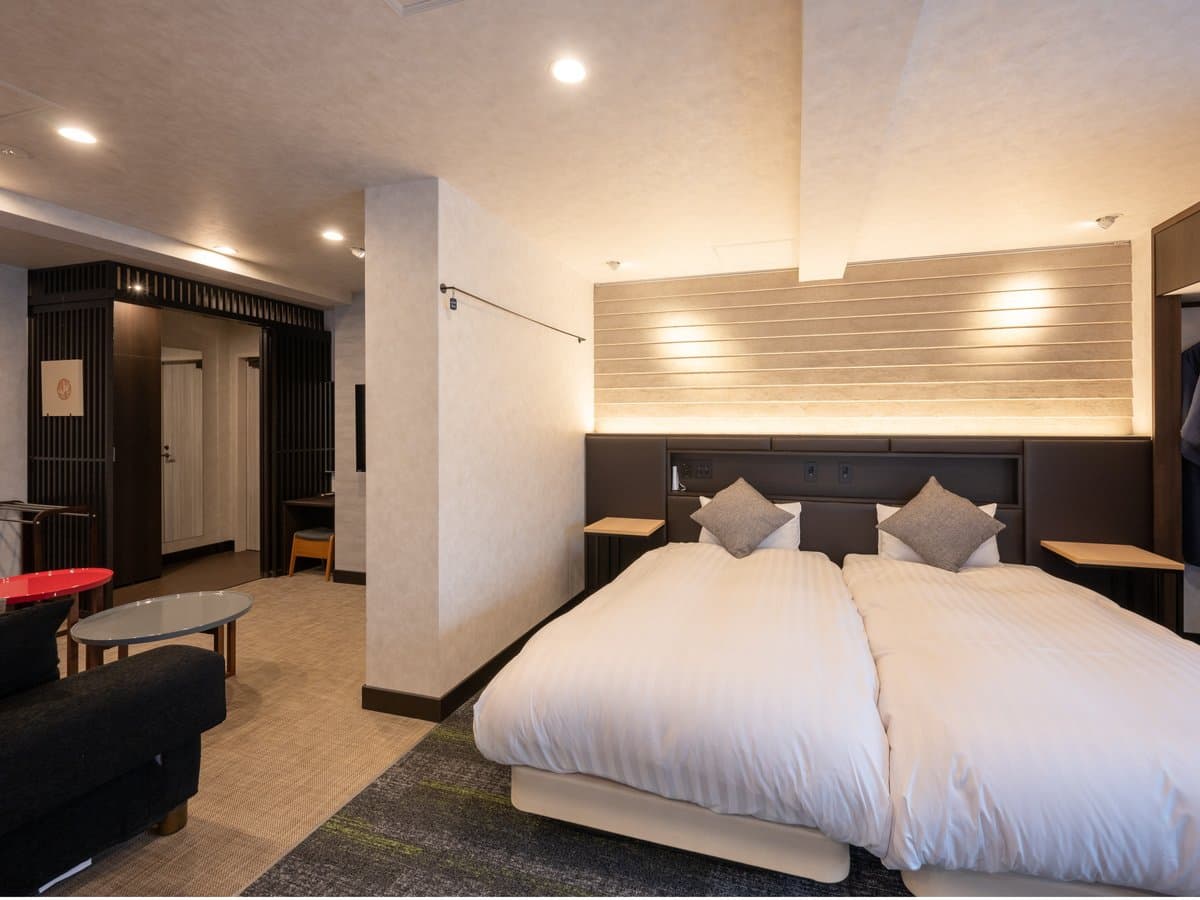 Spacious suite living area with leather sofa, framed artwork and twin beds beyond, Koyado En, Kinosaki Onsen