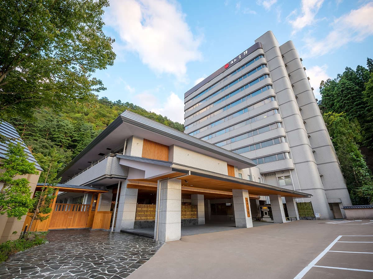 Daytime exterior of the tower hotel and timber entrance porte-cochere set against forested hills, Yumoto Kissho, Naruko Onsen