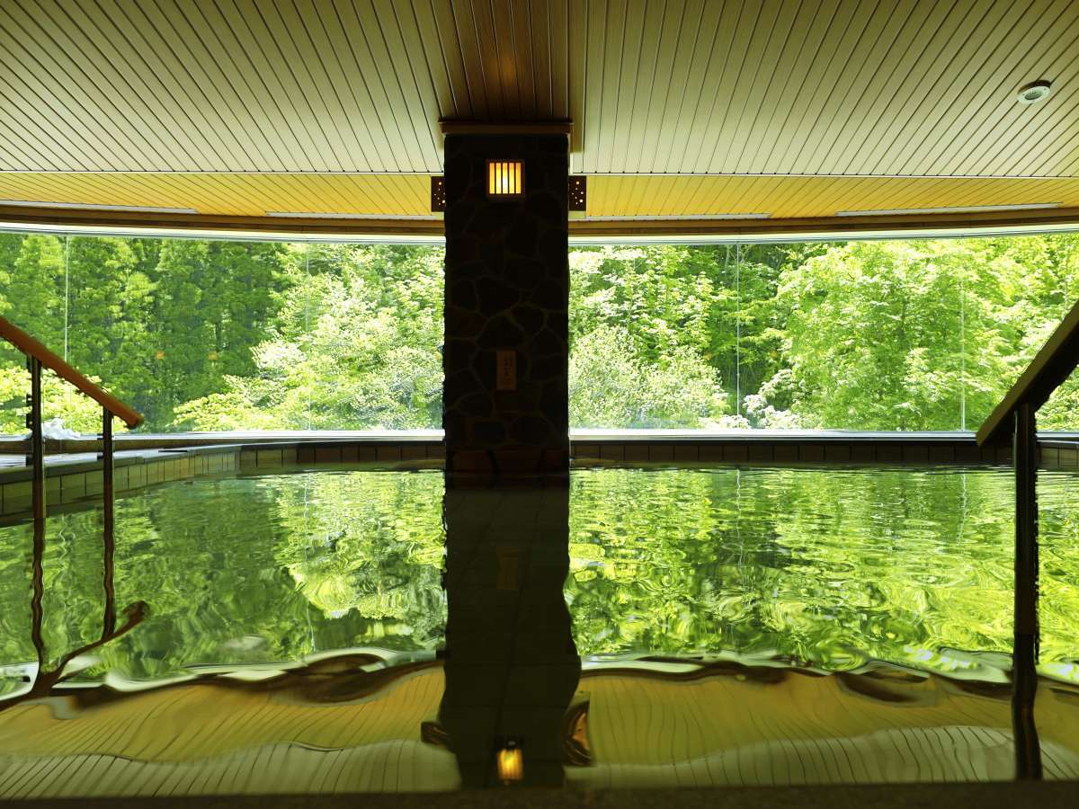 Tranquil indoor stone bath reflecting bright green woodland through panoramic windows, Yumoto Kissho, Naruko Onsen