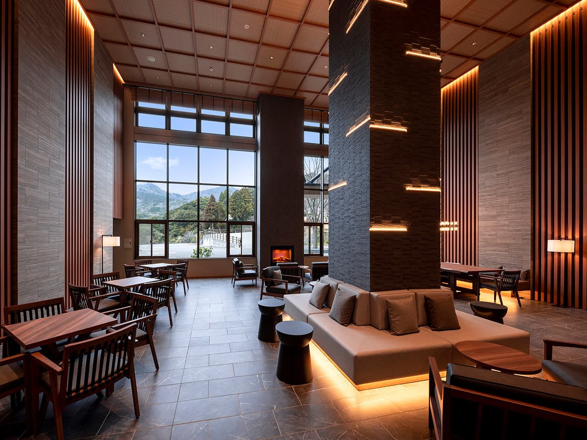 Double-height lobby lounge at Seiunso with a fireplace, low sofa and tall windows overlooking the Unzen mountains