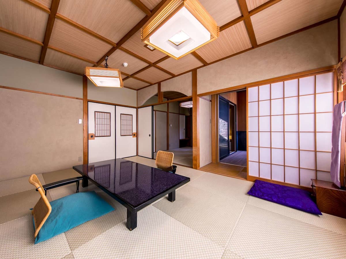 Spacious tatami guest suite with low lacquered table, shoji screens and floor cushions at Ryokan Tachibana