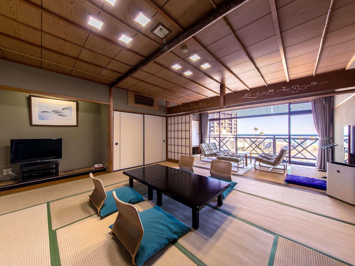 Large sea-view tatami room with rattan chairs and a sunlit balcony at Ryokan Tachibana in Atami