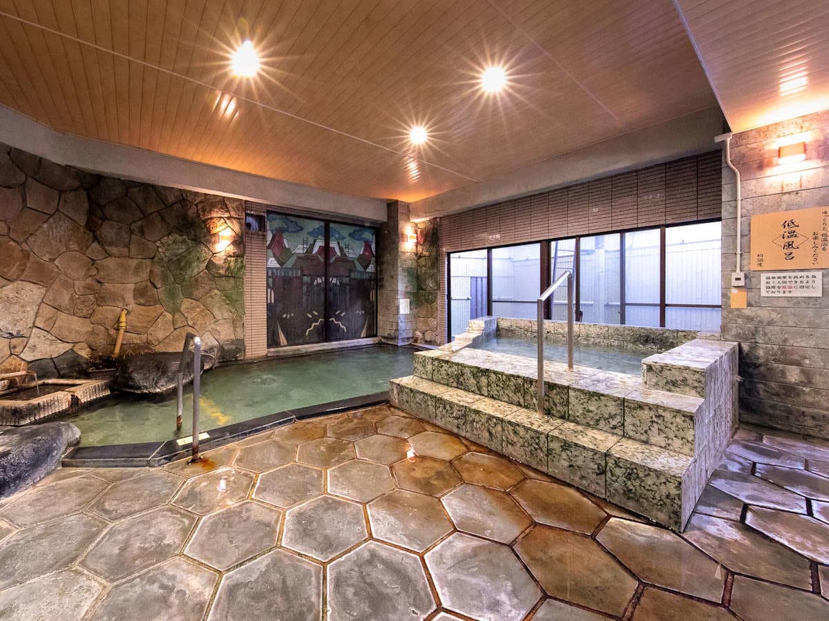 Indoor hot spring bath with natural stone walls and hexagonal floor tiles at Ryokan Tachibana in Atami