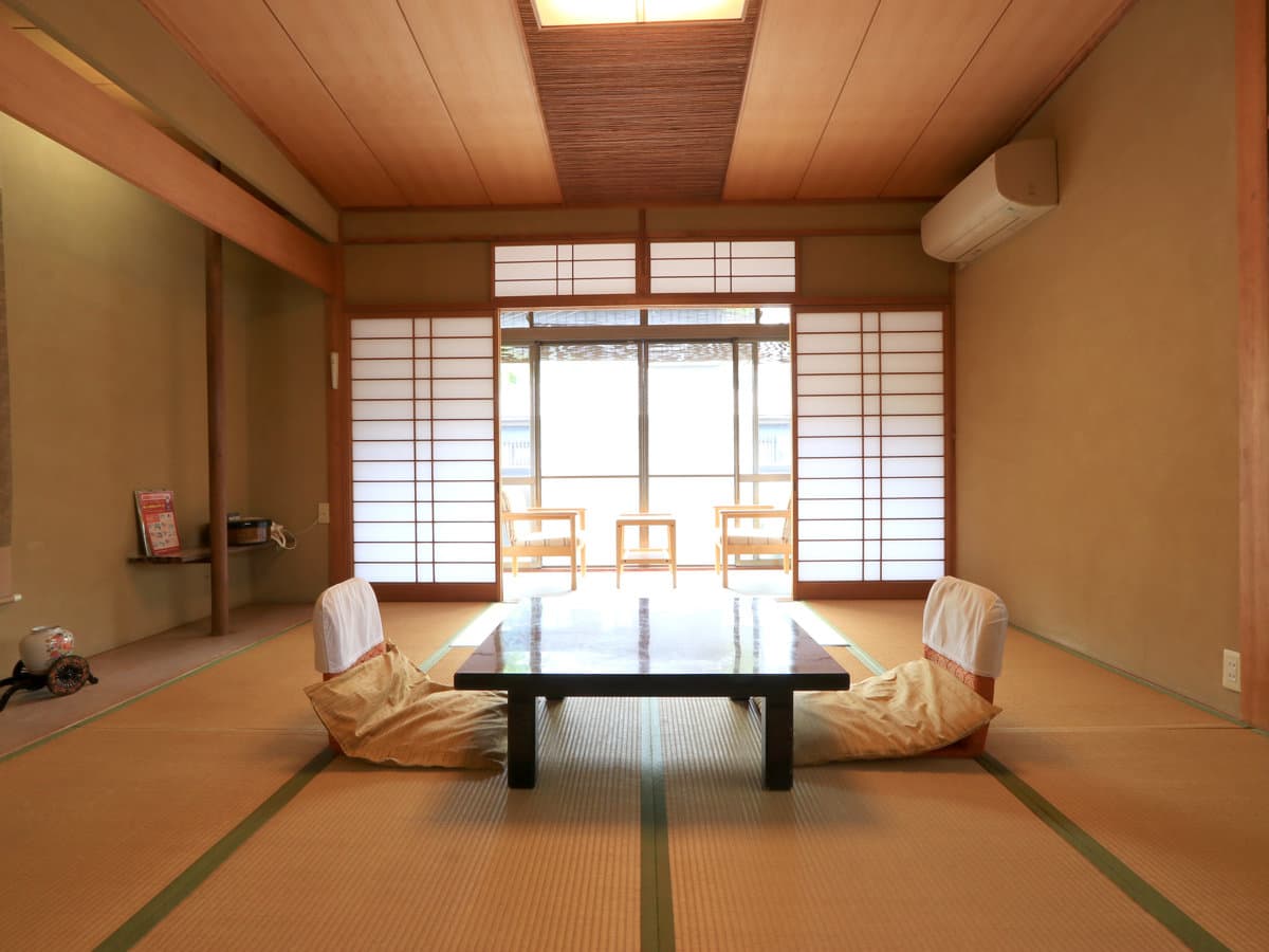 Bright tatami guest room at Kamiobo with a low black-lacquer table, cushioned chairs and shoji opening to garden-view windows