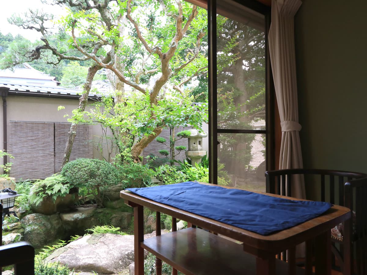 View from a Kamiobo guest room over a small Japanese garden with a maple, stone lantern and clipped shrubs through a wide window