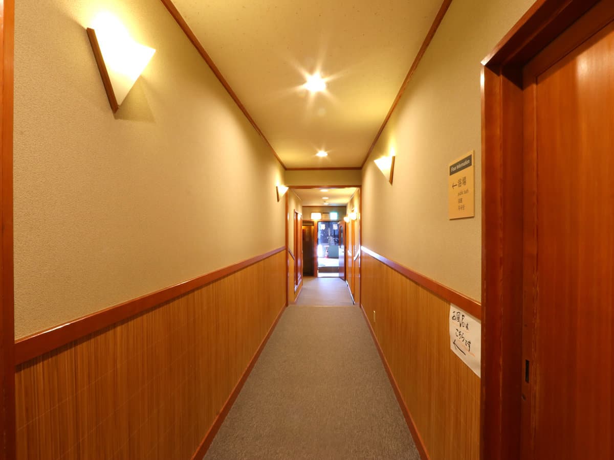Warmly lit interior corridor at Kamiobo with wood-panel wainscoting and wall sconces leading toward the guest rooms