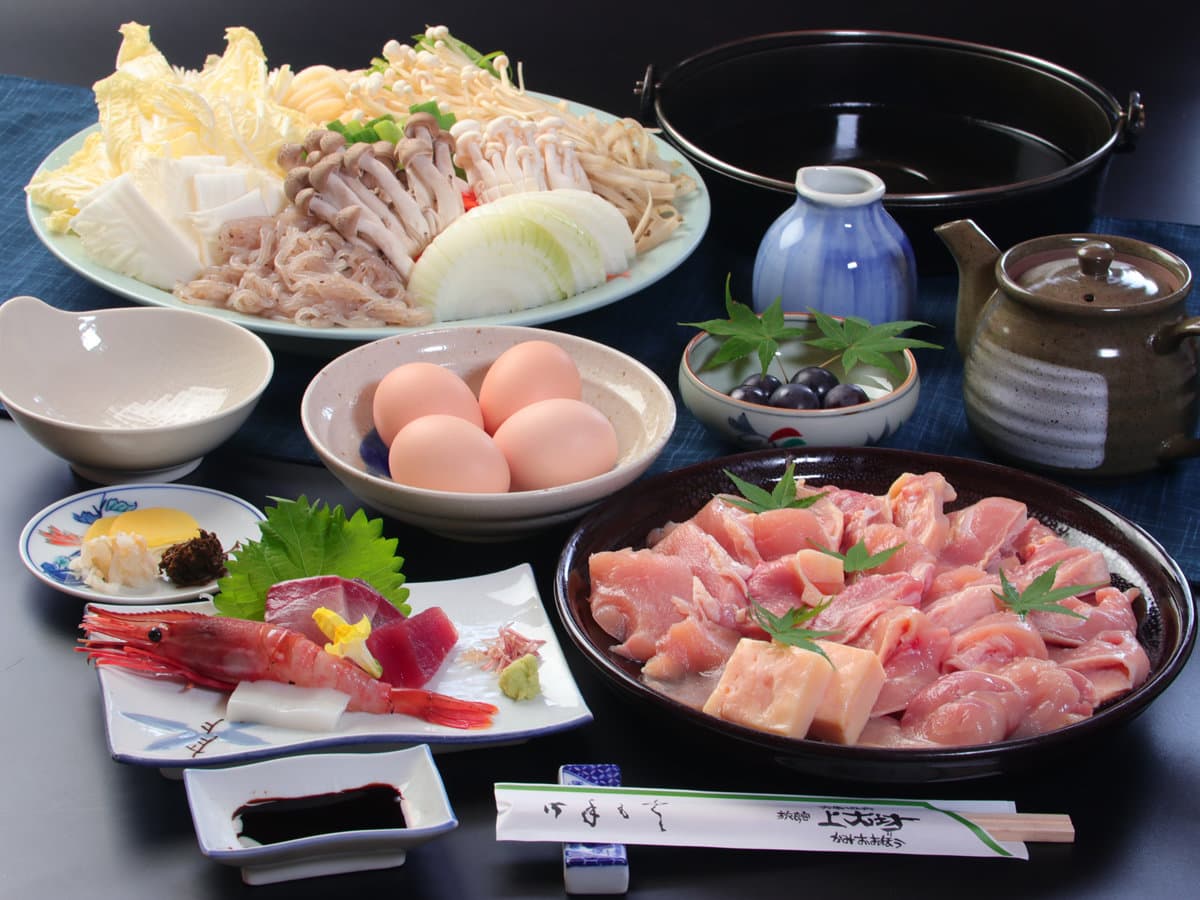 Kaiseki dinner at Kamiobo with marbled beef and chicken for hot pot, a platter of mushrooms and vegetables, sashimi of prawn and tuna, and farm eggs on a dark table