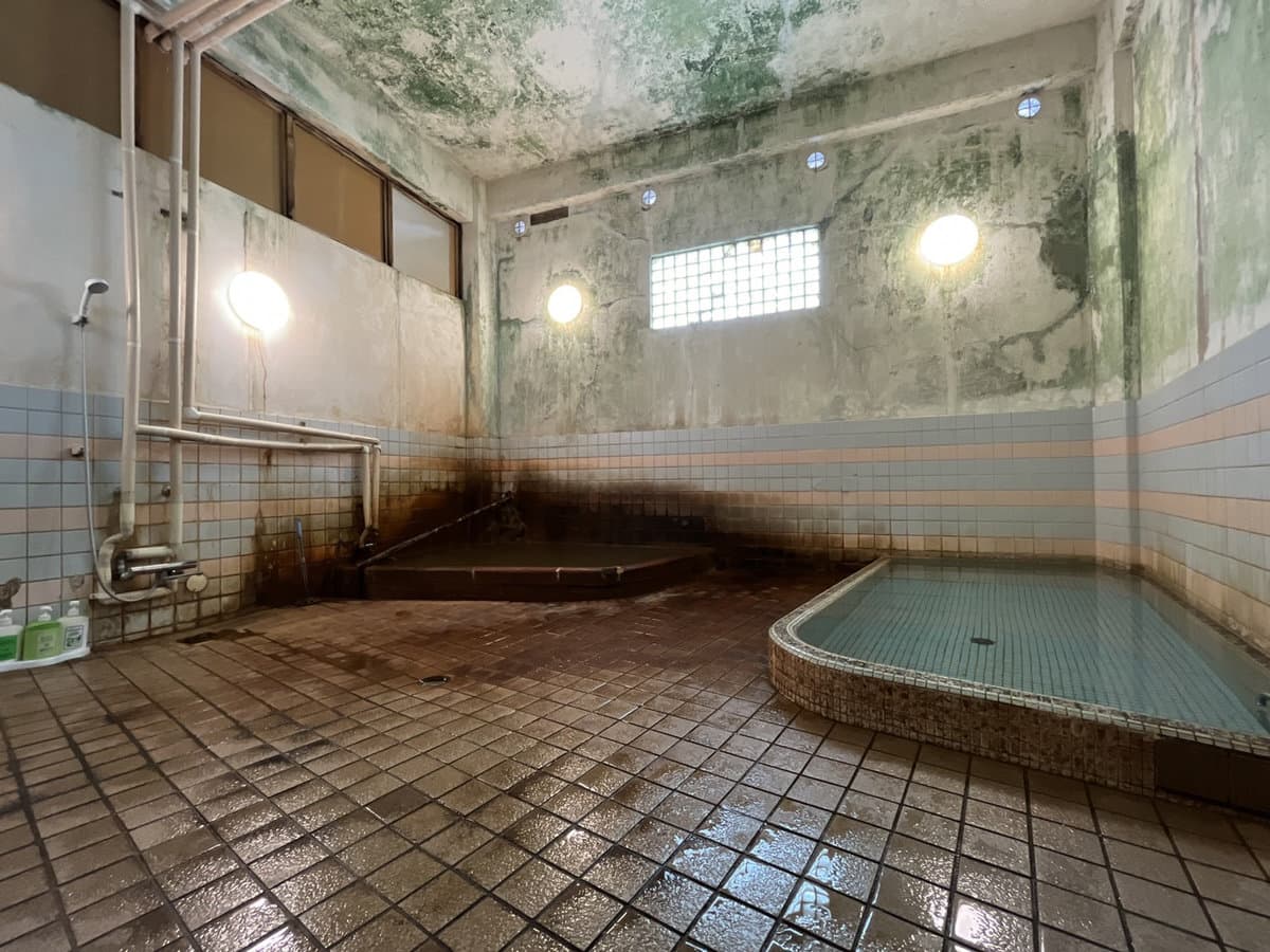 Wide view of Kamiobo's indoor kinsen bathhouse with tiled tubs of golden-brown iron-rich Arima hot spring water and aged plaster walls