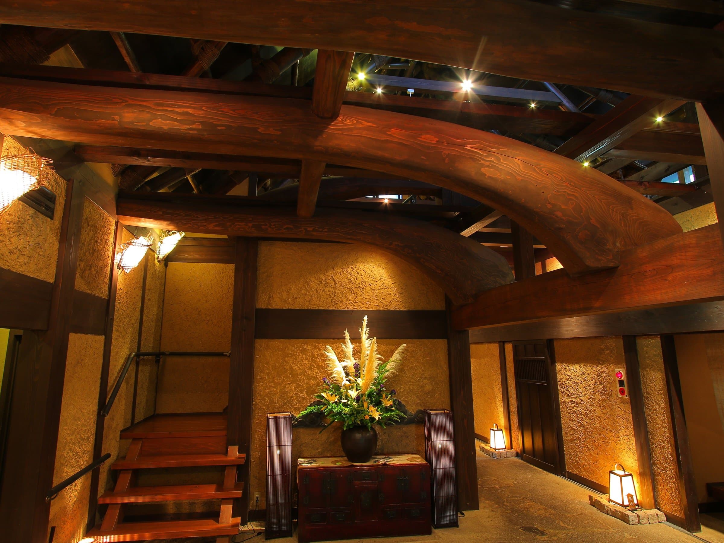 Lobby entrance with curved timber beams, earthen walls and a floral display at Tsuki no Usagi, Izu-Kogen