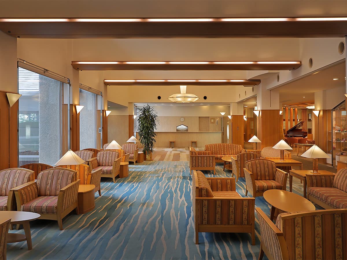 Spacious hotel lobby lounge with armchairs, table lamps and a flowing blue patterned carpet