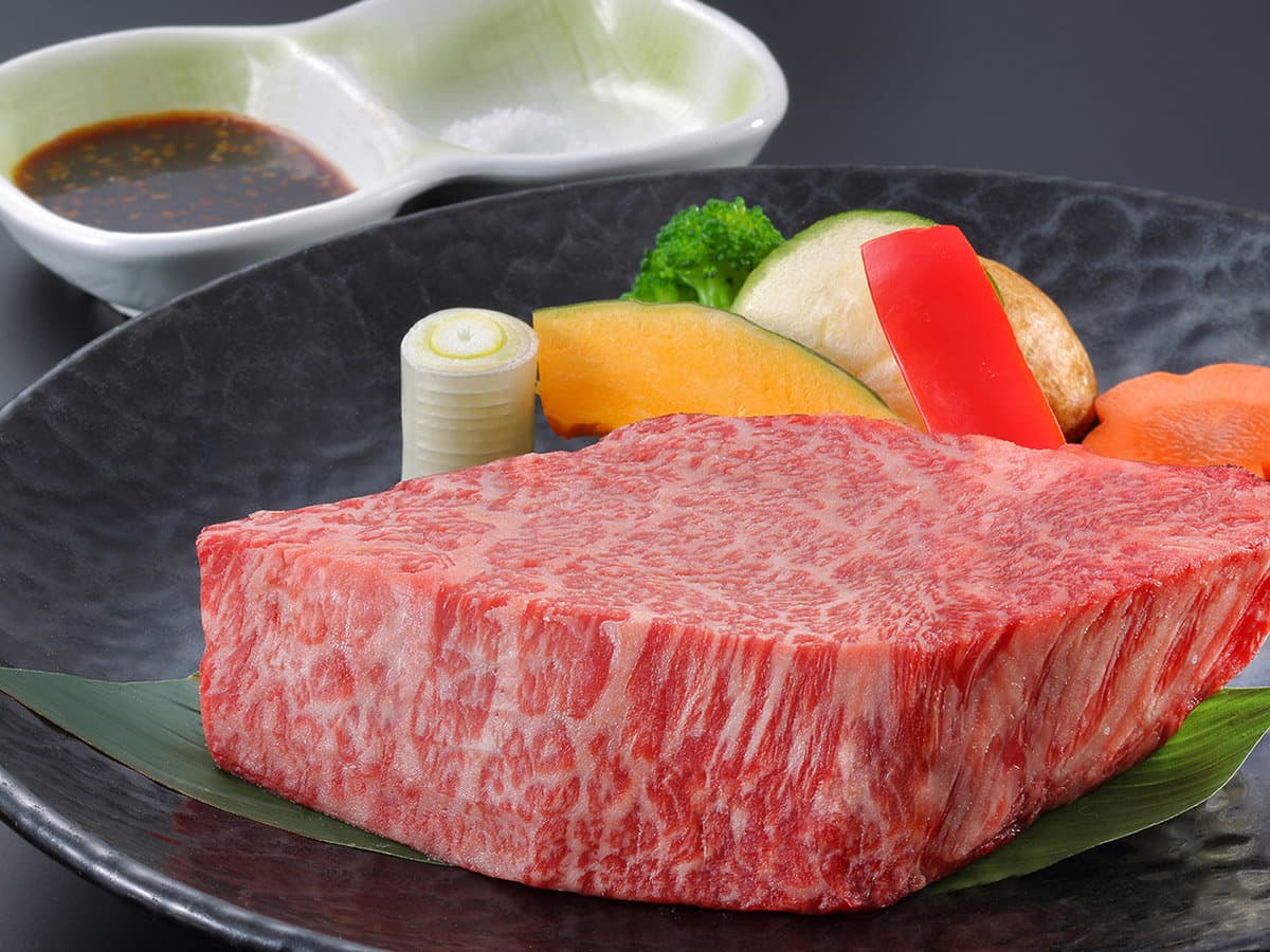 Thick cut of marbled Yamagata wagyu beef steak plated with grilled vegetables and dipping sauce