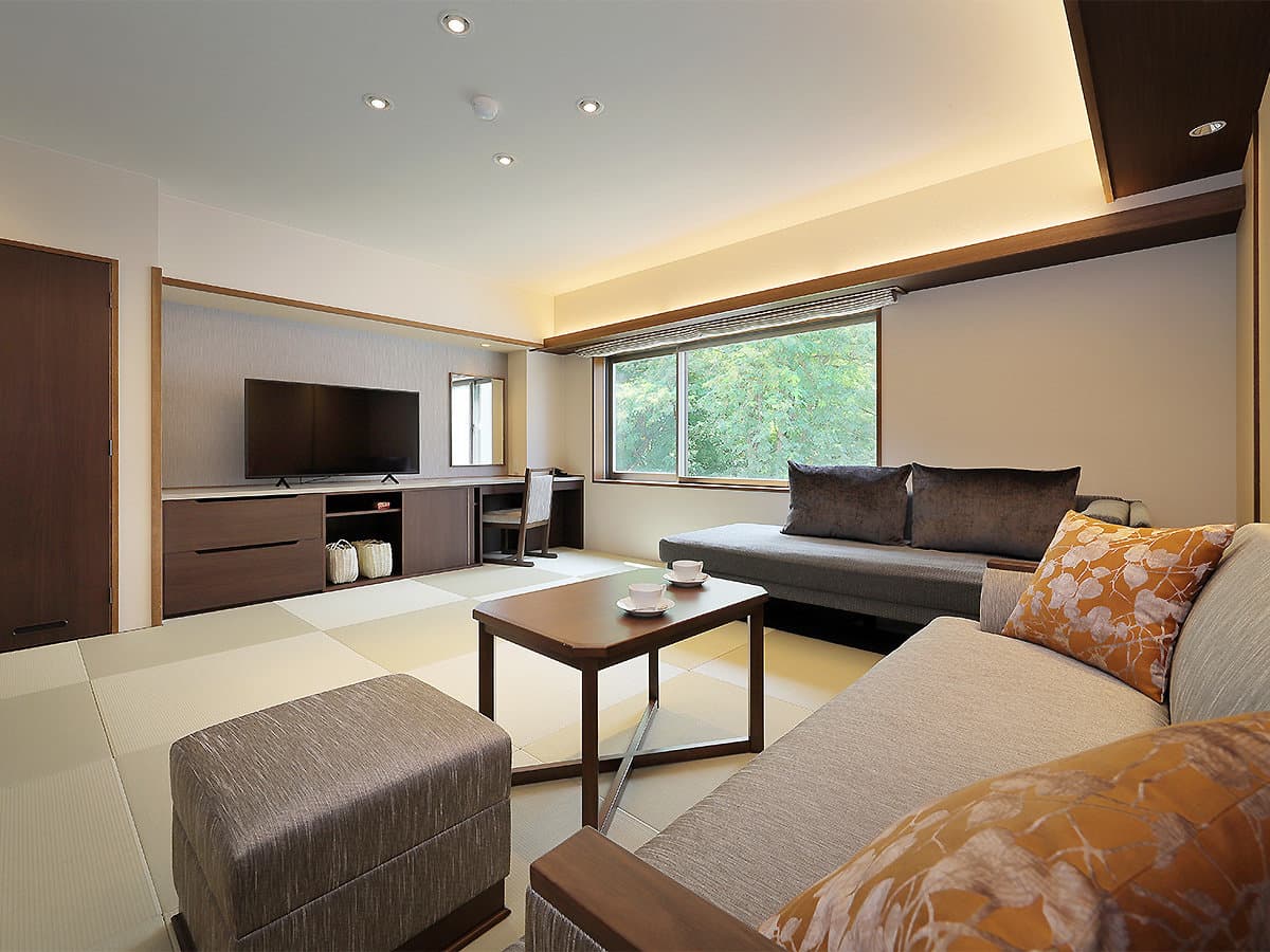 Modern tatami guest room with a low table, sofa and large window overlooking green forest