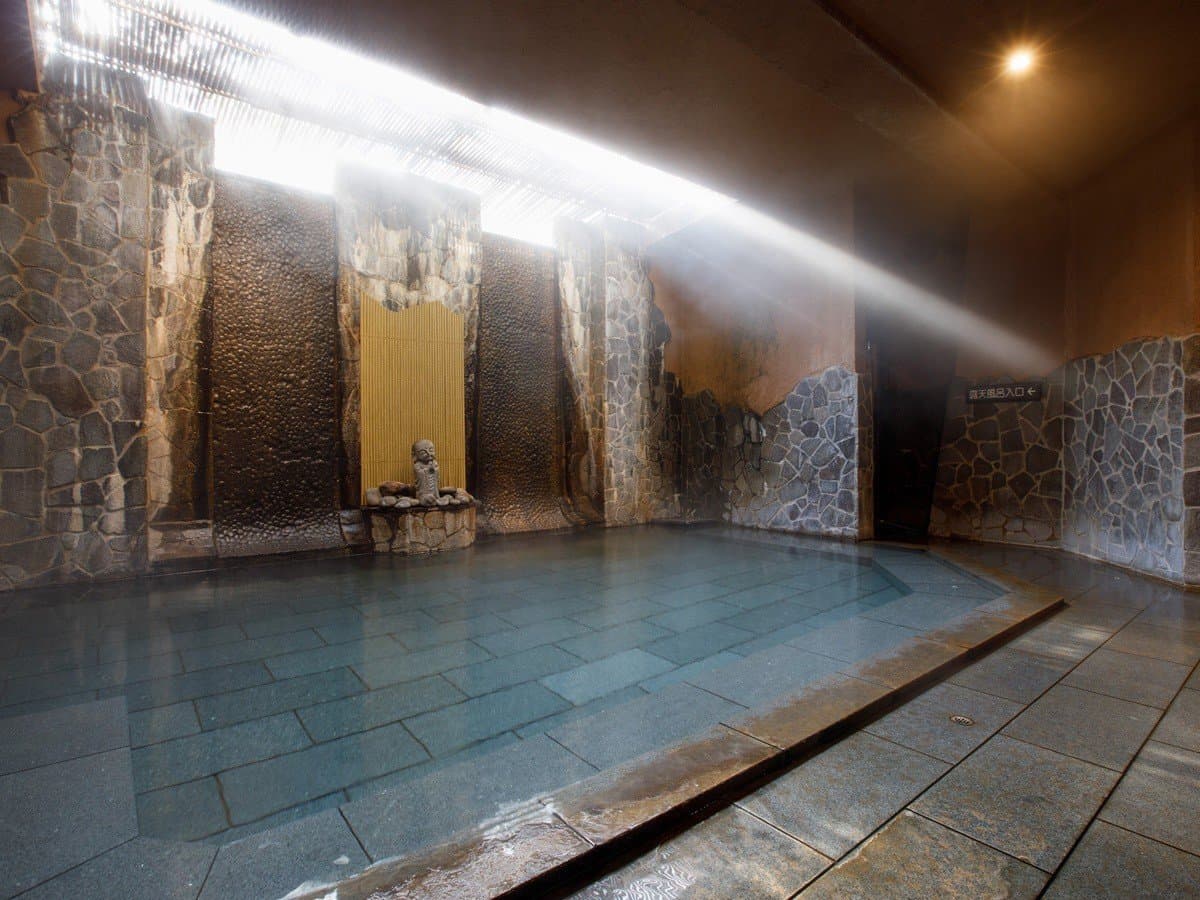 Yusai stone-walled indoor onsen bath with rising steam and rugged rock surrounds