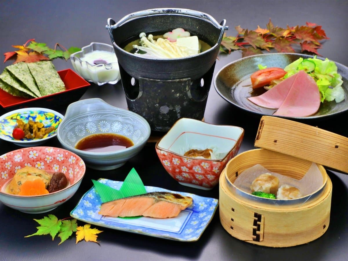 Multi-course Japanese dinner spread with small hot pot, grilled fish, simmered dishes and steamed shumai