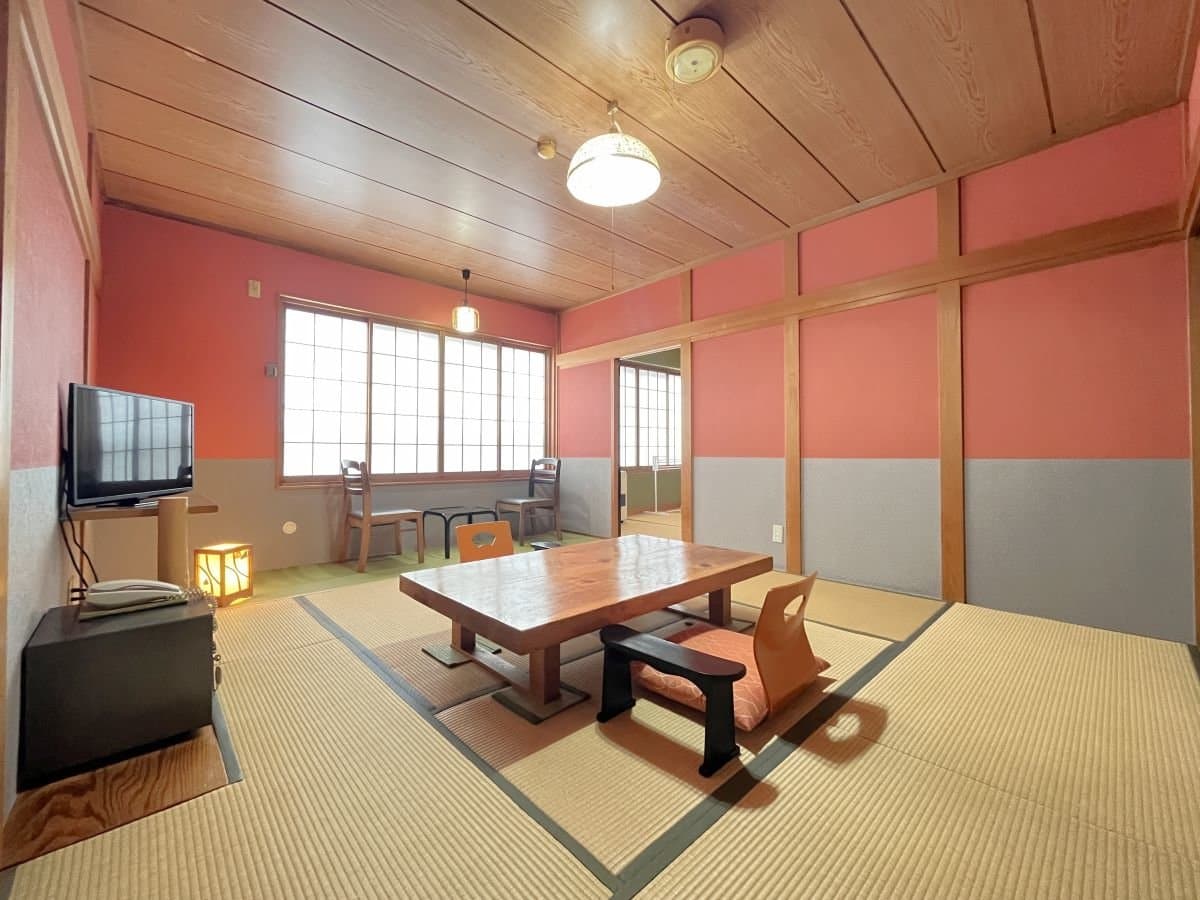 Spacious tatami guest room with pink walls, a low wooden table, floor chairs and a window seating area
