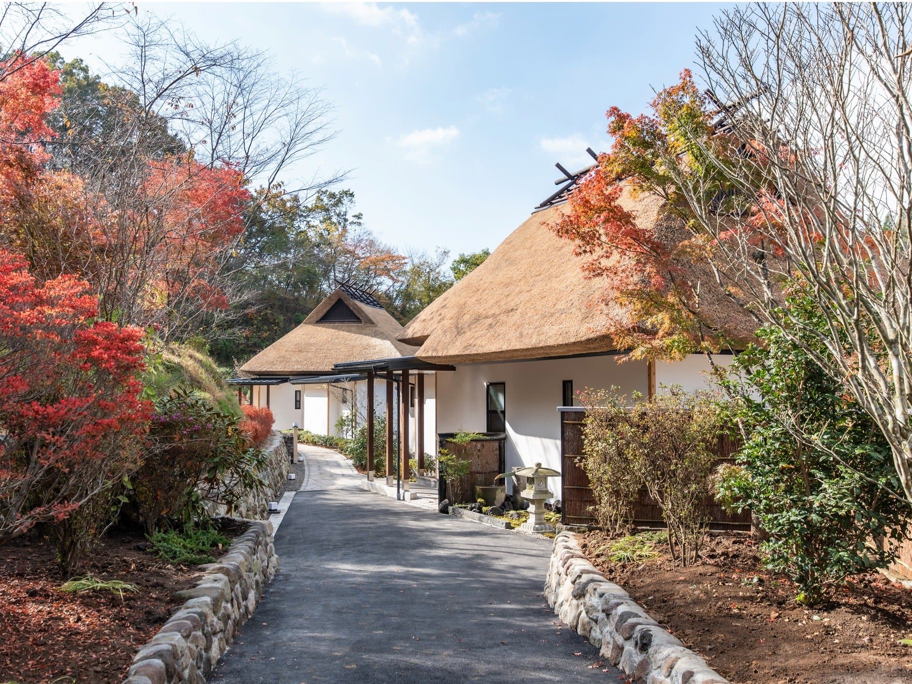 Daytime exterior of Miyama Sansou's thatched-roof main building with a stone-lined approach path framed by autumn foliage